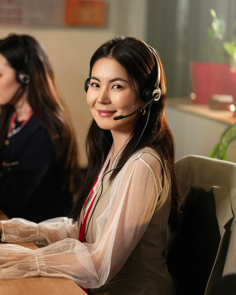 Atendente com headset sorrindo em frente ao computador, numa central de atendimento