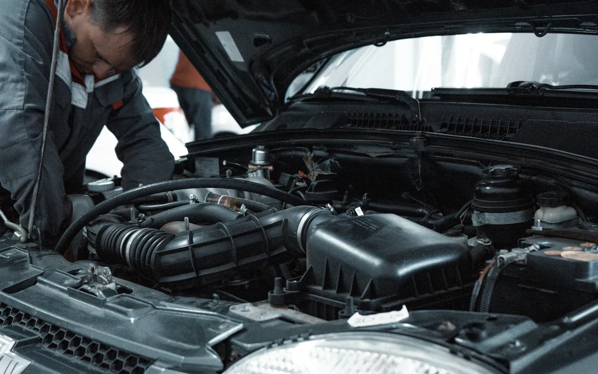 Mecânico de uniforme inspecionando o motor de um carro na oficina